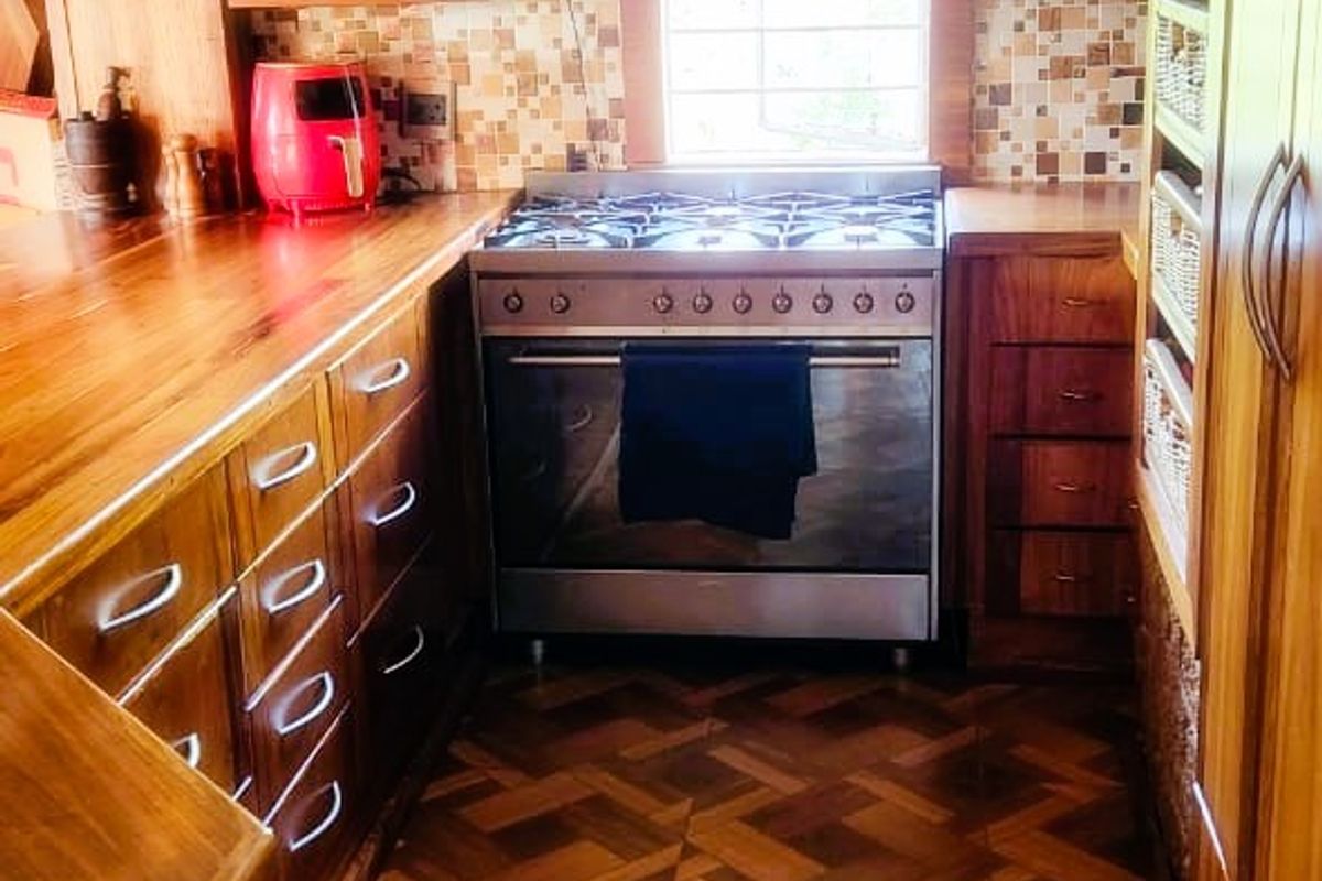 A compact kitchen featuring warm wooden cabinetry, wooden countertops, a gas stove with extractor fan, and patterned tiled flooring.