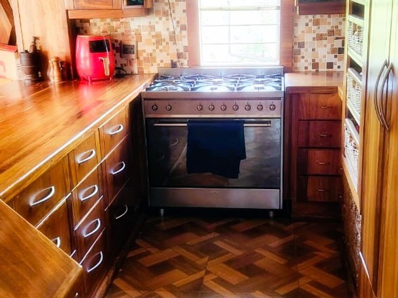 A compact kitchen featuring warm wooden cabinetry, wooden countertops, a gas stove with extractor fan, and patterned tiled flooring.