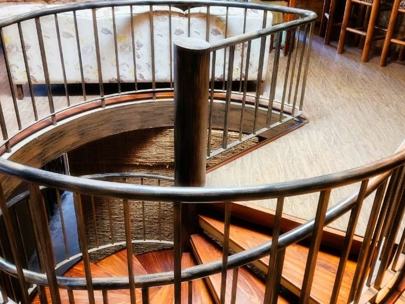 A view of a spiral staircase with timber treads and a metal balustrade, situated within an open living area with wood-look flooring.