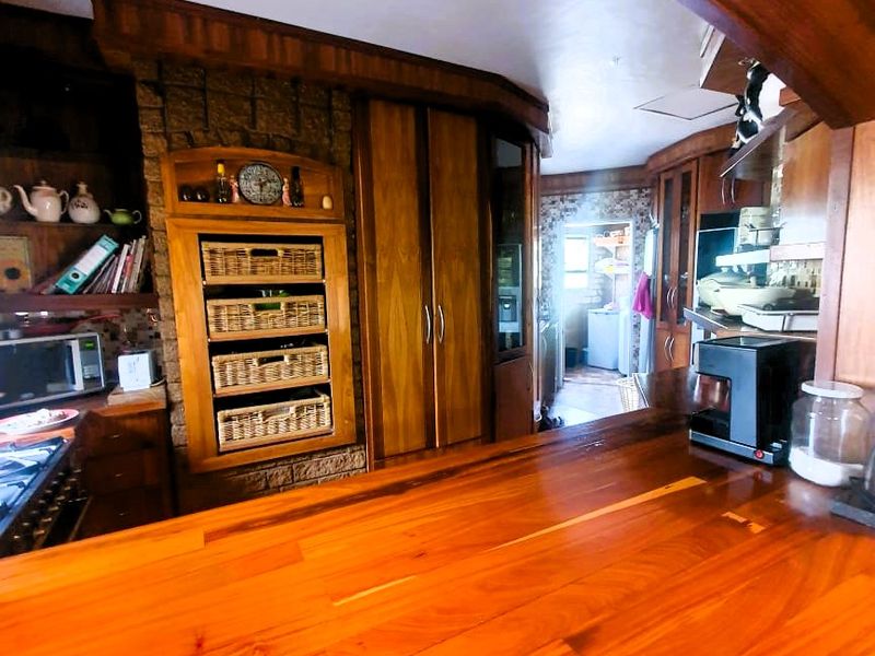 A rustic kitchen featuring extensive wooden cabinetry, a stone feature wall, and a large wooden breakfast bar with integrated lighting.