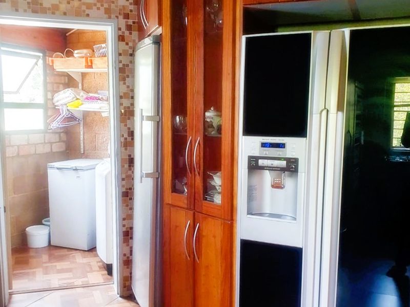 Kitchen area featuring warm-toned wooden cabinetry, mosaic wall tiles, and tiled flooring, with an adjacent utility space visible through the doorway.
