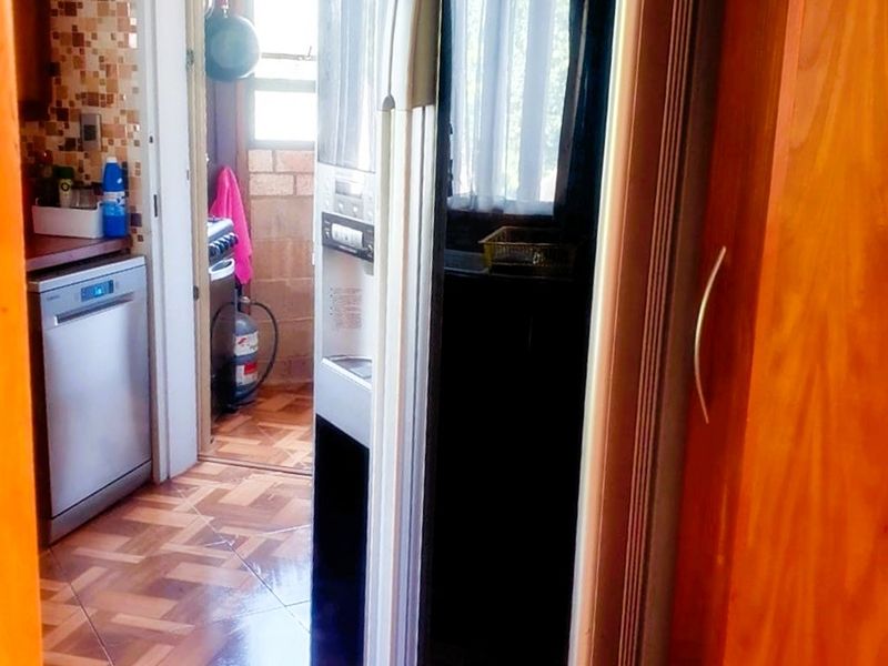A functional kitchen area featuring tiled flooring, mosaic backsplash, and built-in cabinetry, with an adjacent scullery or utility space visible through the doorway.