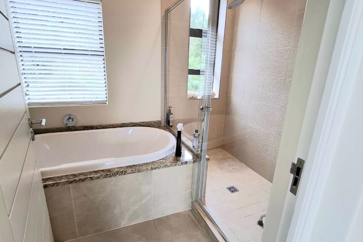 A clean, modern bathroom featuring a built-in bathtub with granite surround, a separate glass-enclosed shower, and neutral floor tiling.