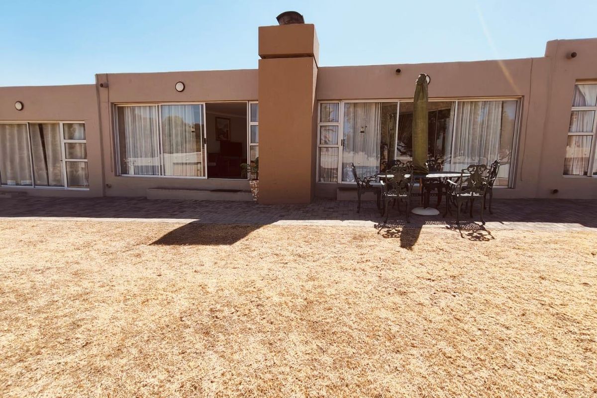 Rear exterior view of the house featuring a paved patio area, large sliding glass doors, and a central chimney stack.