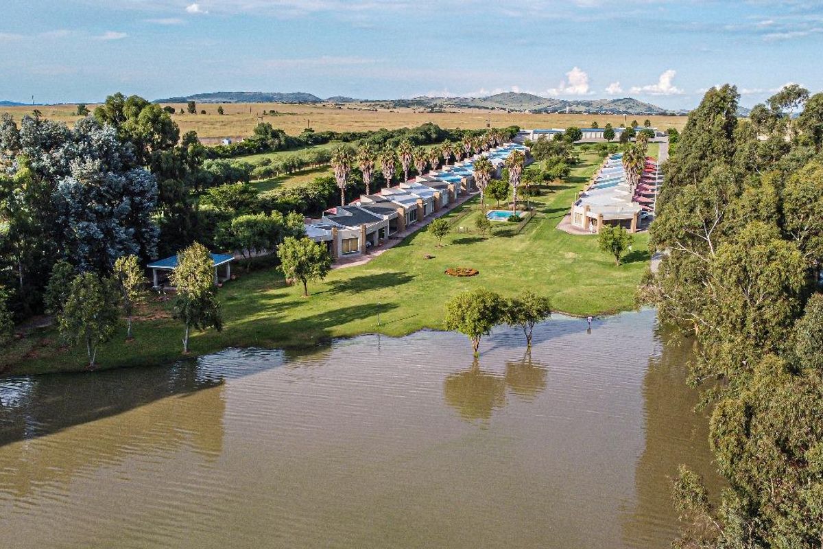 Aerial view of a residential estate featuring multiple units, landscaped grounds, swimming pools, and a large lake in a scenic setting.