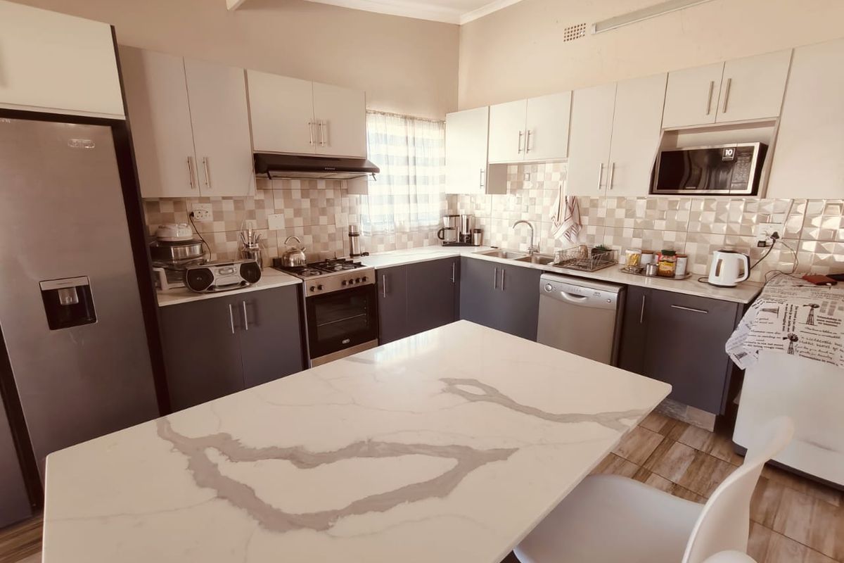 Modern kitchen featuring two-tone cabinetry, stone-topped island, tiled backsplash, and integrated appliances, offering a functional and contemporary cooking space.