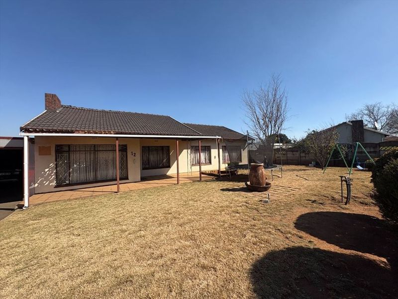 Rear view of the house featuring a covered patio, tiled roof, brick chimney, and a spacious garden with perimeter walling.