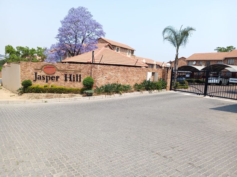 Front entrance view of Jasper Hill townhouse complex featuring a brick boundary wall, paved driveway, and secure gated access.