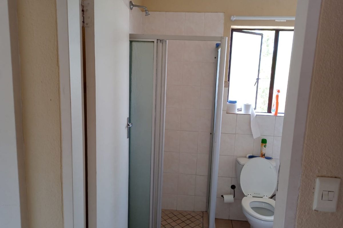 A functional bathroom featuring a shower enclosure, toilet, and tiled finishes, offering a blank canvas for potential modernization and renovation.