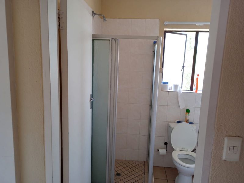 A functional bathroom featuring a shower enclosure, toilet, and tiled finishes, offering a blank canvas for potential modernization and renovation.