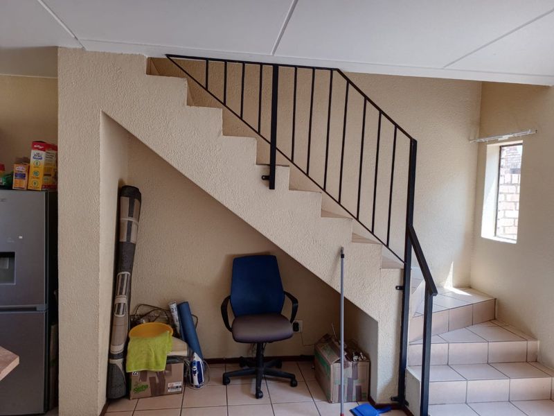 A hallway area featuring a staircase with a metal balustrade and tiled flooring, providing access to the upper level of the townhouse.