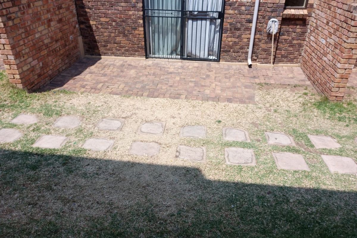 Rear exterior area featuring a brick-paved patio, sliding glass door with security gate, and a garden path with stepping stones.
