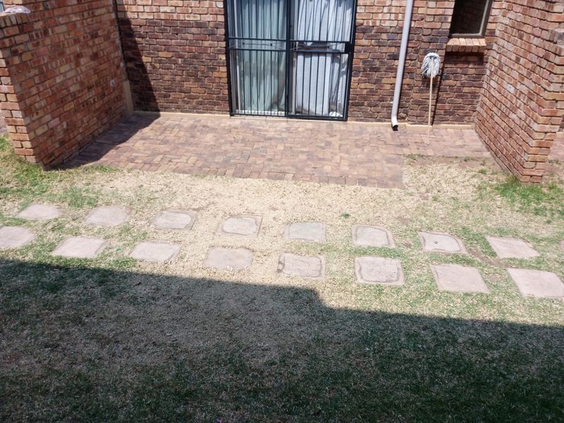Rear exterior area featuring a brick-paved patio, sliding glass door with security gate, and a garden path with stepping stones.