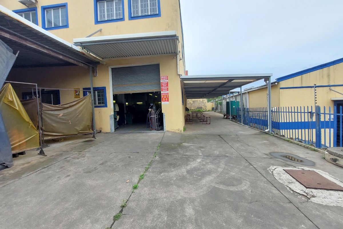 Industrial rear exterior area featuring a concrete driveway, roller shutter access, and a covered loading or storage canopy.
