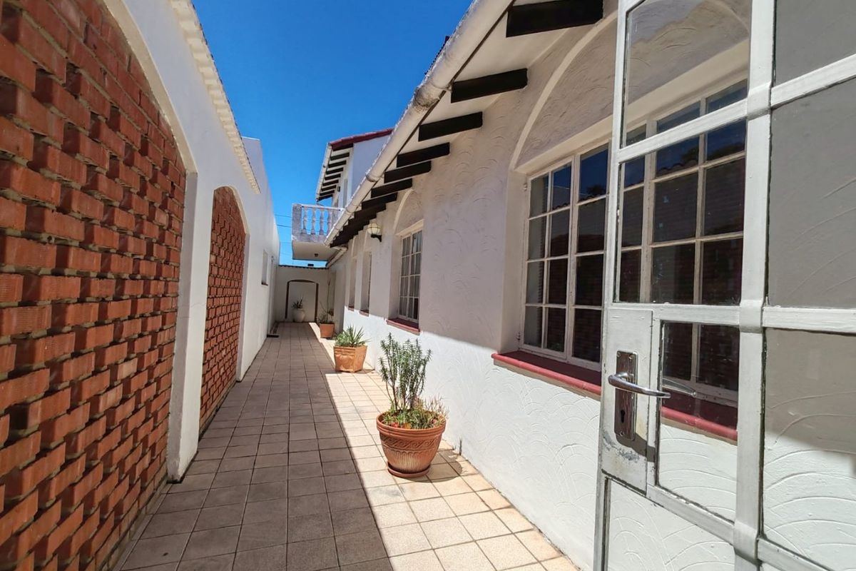 A paved exterior walkway along the side of the house, featuring exposed brickwork, timber rafters, and white-painted walls with multi-pane windows.