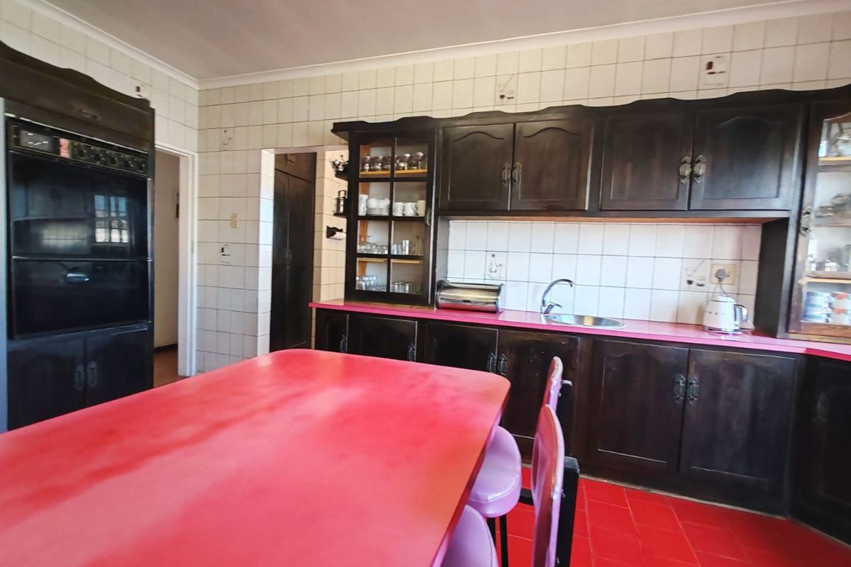A dated kitchen featuring dark wood cabinetry, a double wall oven, tiled splashbacks, and a bright red countertop and floor.