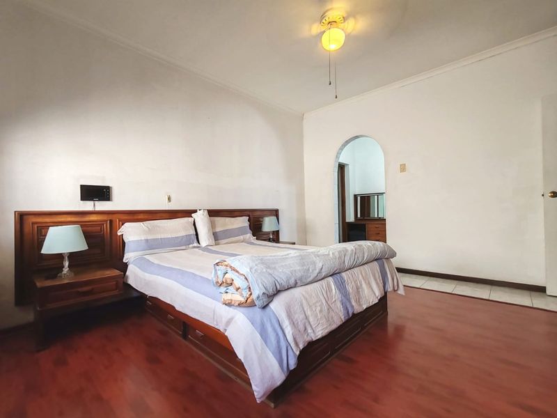Spacious bedroom featuring laminate flooring, a built-in wooden headboard, and an arched doorway leading to an adjoining space.
