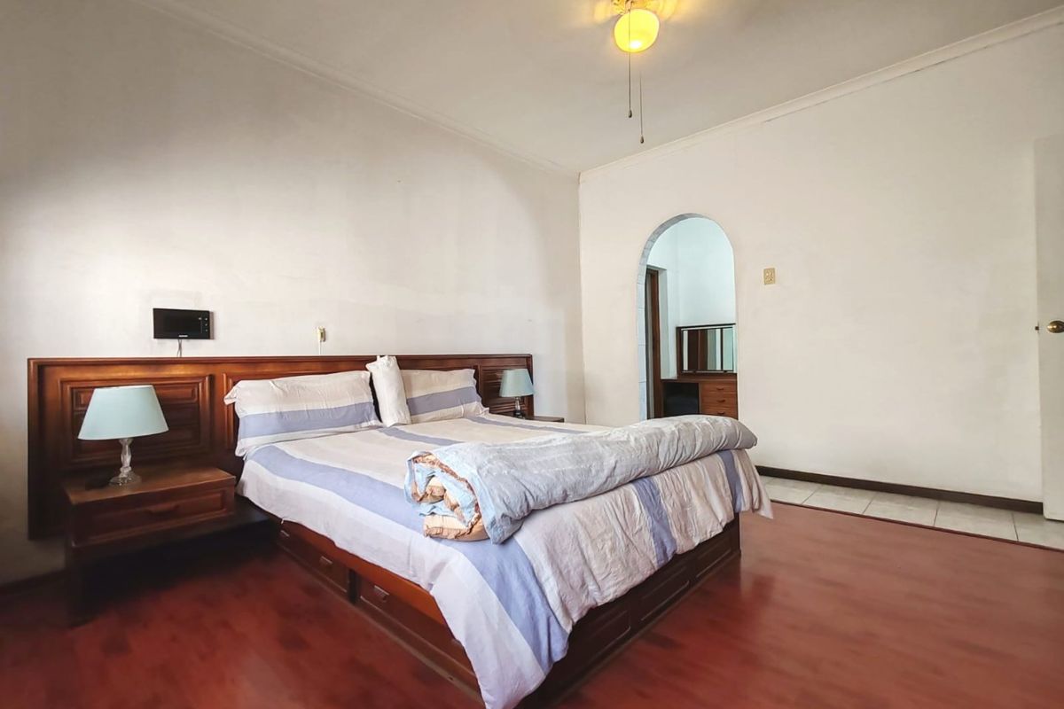 Spacious bedroom featuring laminate flooring, a built-in wooden headboard, and an arched doorway leading to an adjoining space.