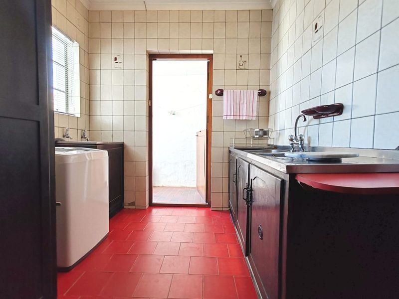 A functional laundry room featuring tiled walls, red tiled flooring, built-in cabinetry, and a stainless steel sink with direct access to an outdoor area.