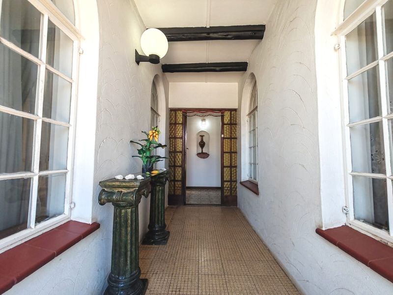 A bright, arched hallway featuring exposed ceiling beams, tiled flooring, and a decorative wall niche, providing a classic architectural transition between living spaces.