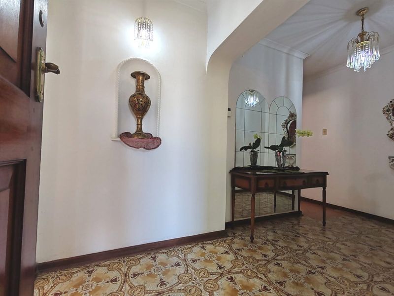 Welcoming entrance hall featuring ornate patterned floor tiles, an arched transition, decorative wall niche, and elegant crystal chandelier lighting.