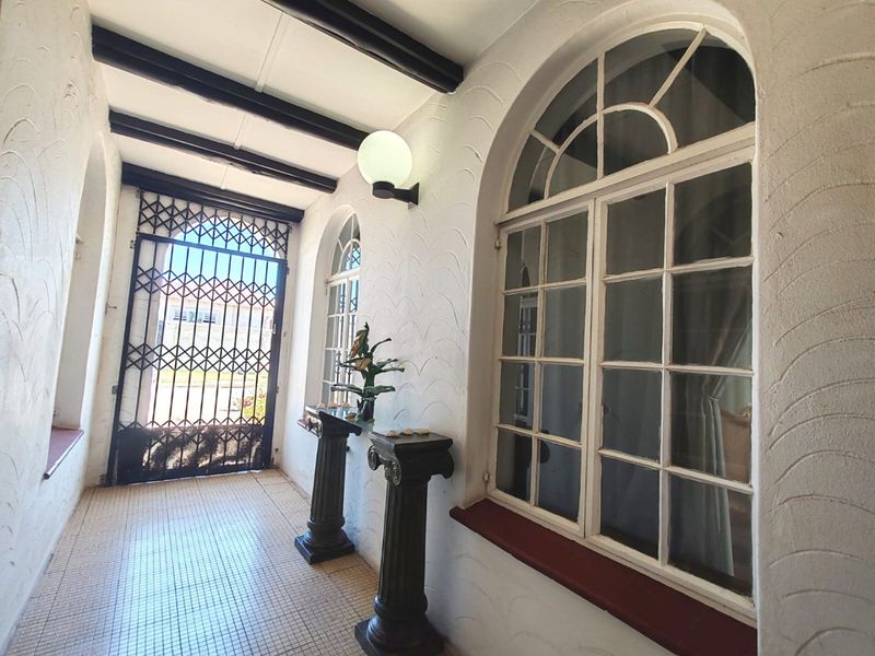 A bright, covered entrance area featuring arched windows, exposed ceiling beams, and secure metal gate access, finished with tiled flooring.