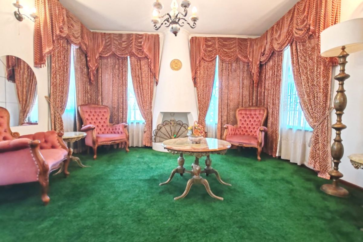 A formal living room featuring a central built-in fireplace, ornate chandelier, and wall sconces, currently finished with dated green carpeting.