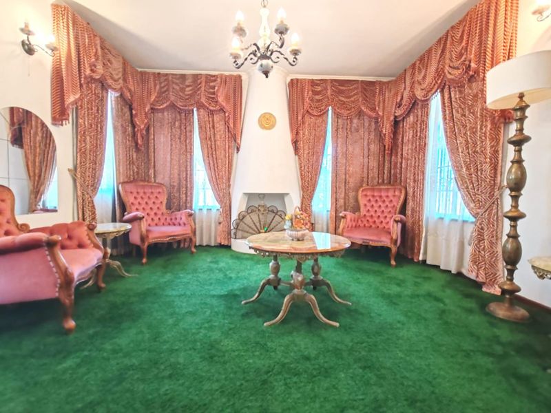 A formal living room featuring a central built-in fireplace, ornate chandelier, and wall sconces, currently finished with dated green carpeting.