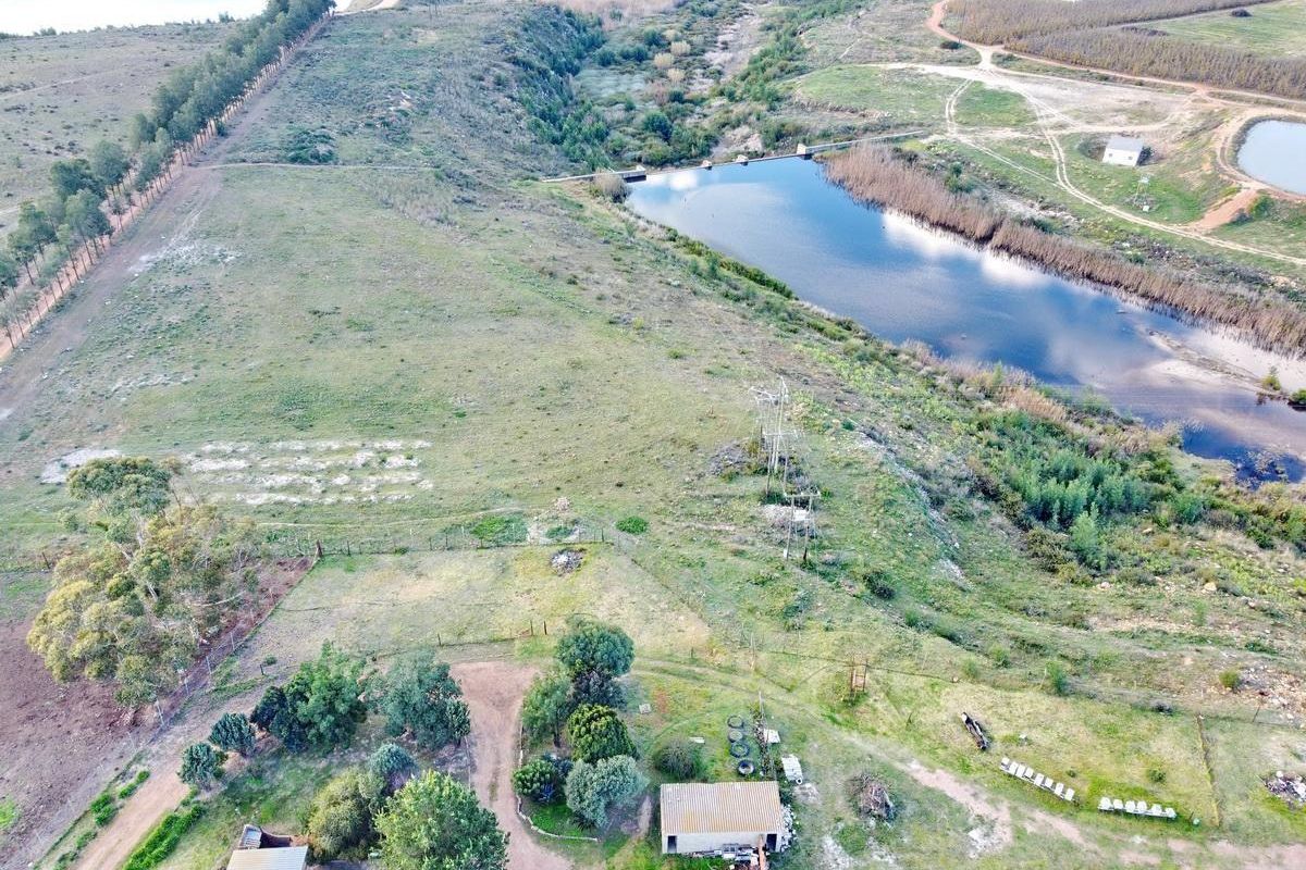 Aerial view of the farm property featuring open grazing land, a large dam, and existing outbuildings.