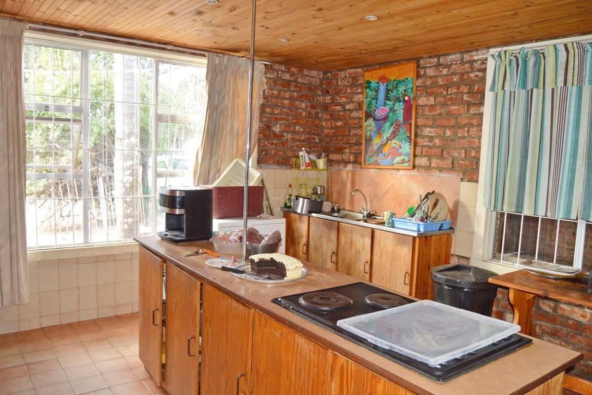 A rustic kitchen featuring exposed brick walls, timber ceiling, wooden cabinetry, and a built-in hob, offering a traditional farm-style aesthetic.