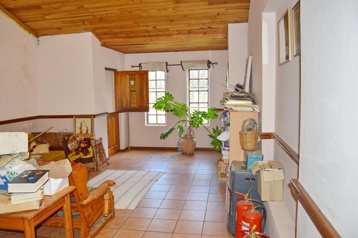 A living area featuring a timber-clad ceiling, tiled flooring, and timber-framed windows, requiring cosmetic updates to the wall finishes.