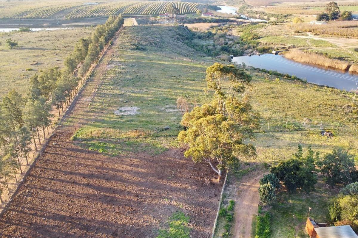 Aerial view of the farm property featuring open fields, established trees, a river, and a dam, showcasing the expansive agricultural landscape.