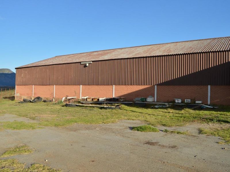A large agricultural shed featuring corrugated metal roofing and brick masonry walls, situated on a rural property with open ground.