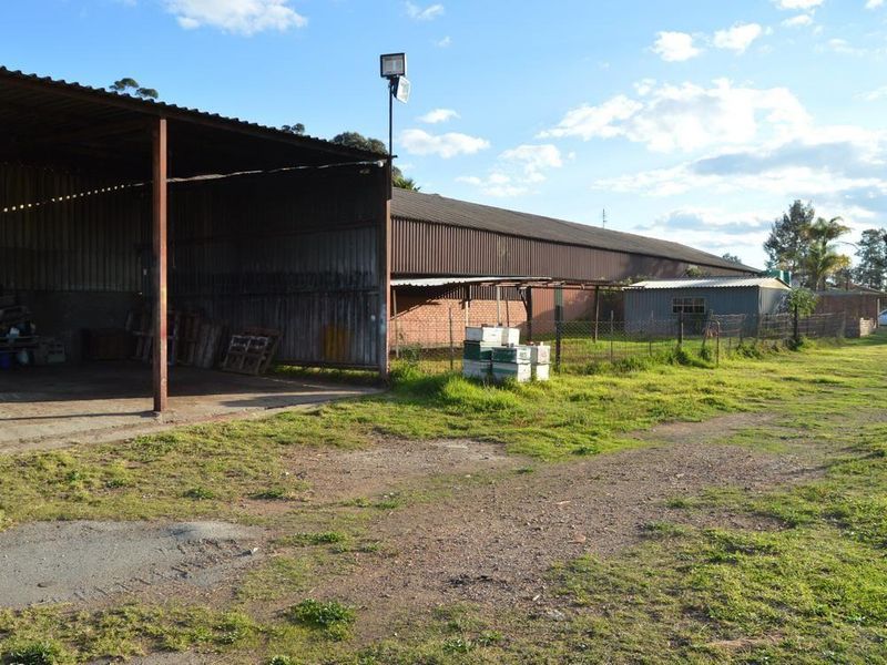 Exterior view of a large farm shed with corrugated metal roofing, steel support structure, and an adjacent open-air storage area on a grass lot.