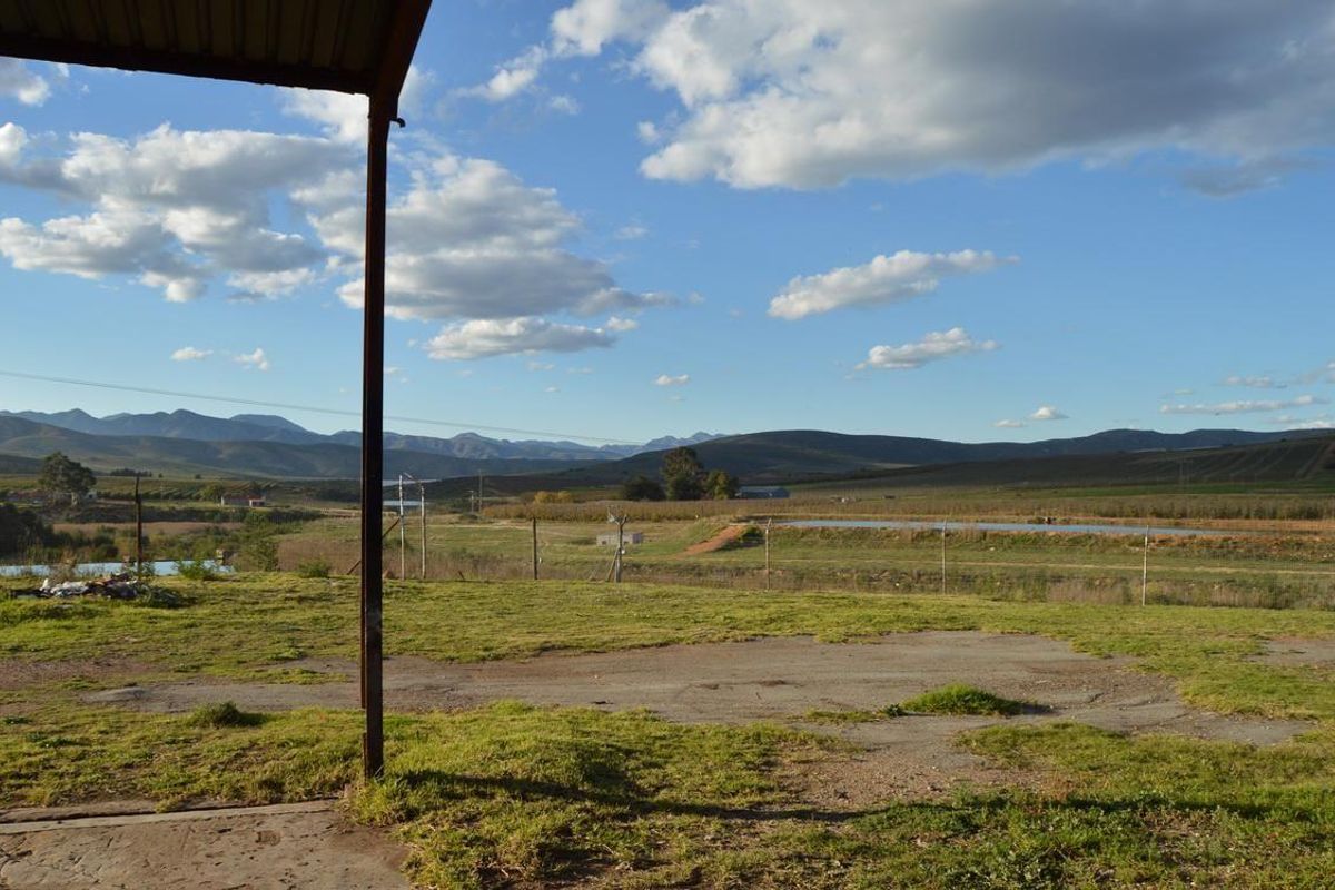 Expansive rural landscape view featuring mountain vistas, open fields, and a covered patio area with a metal support structure.