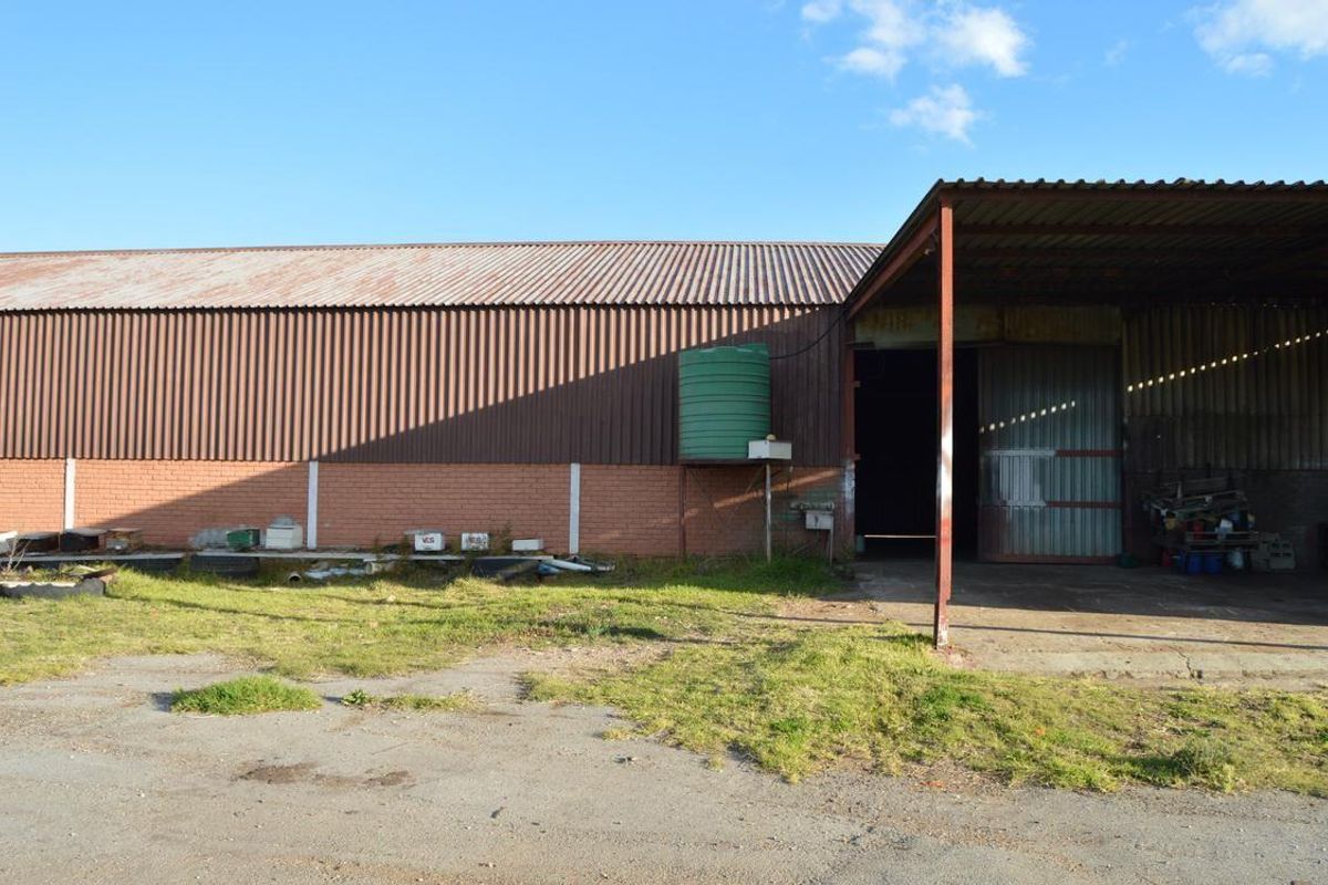 A large agricultural shed featuring corrugated metal roofing, brick walls, a water storage tank, and a covered loading area with a sliding metal door.
