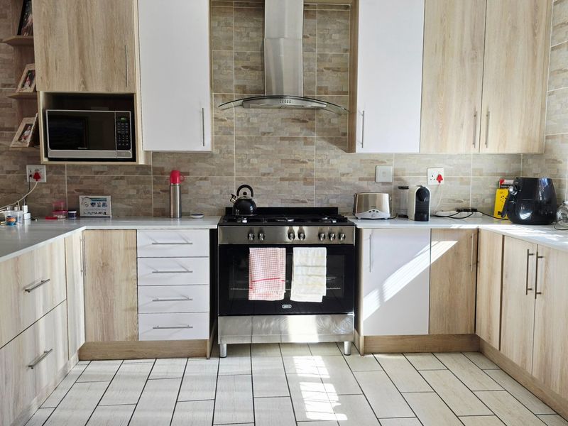 A well-maintained kitchen featuring light wood-grain cabinetry, stone-look wall tiling, a gas stove with extractor fan, and built-in microwave.