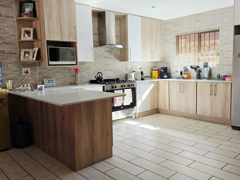 Modern kitchen featuring light wood-tone cabinetry, stone countertops, a gas stove with extractor fan, and tiled finishes throughout.
