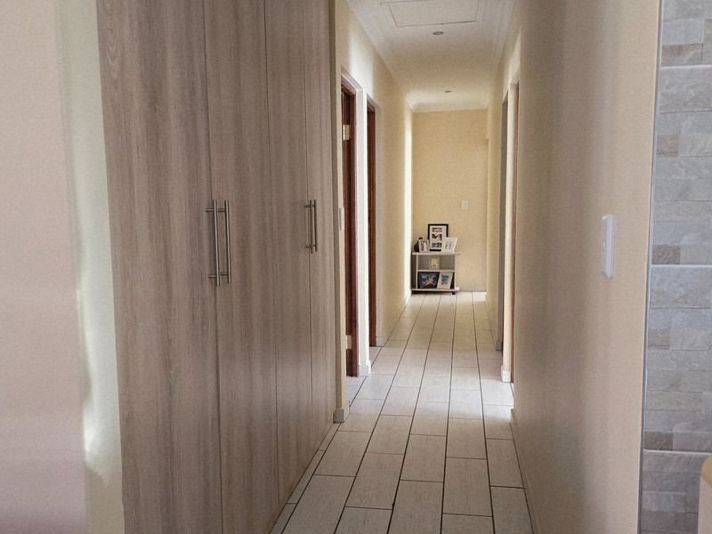 A clean, well-lit hallway featuring light wood-finish built-in cupboards and neutral tiled flooring, providing access to multiple rooms.