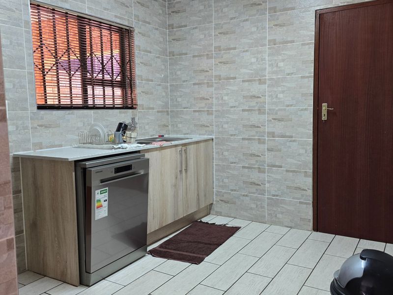 A functional scullery area featuring tiled walls, built-in cabinetry, a stainless steel sink, and an integrated dishwasher.