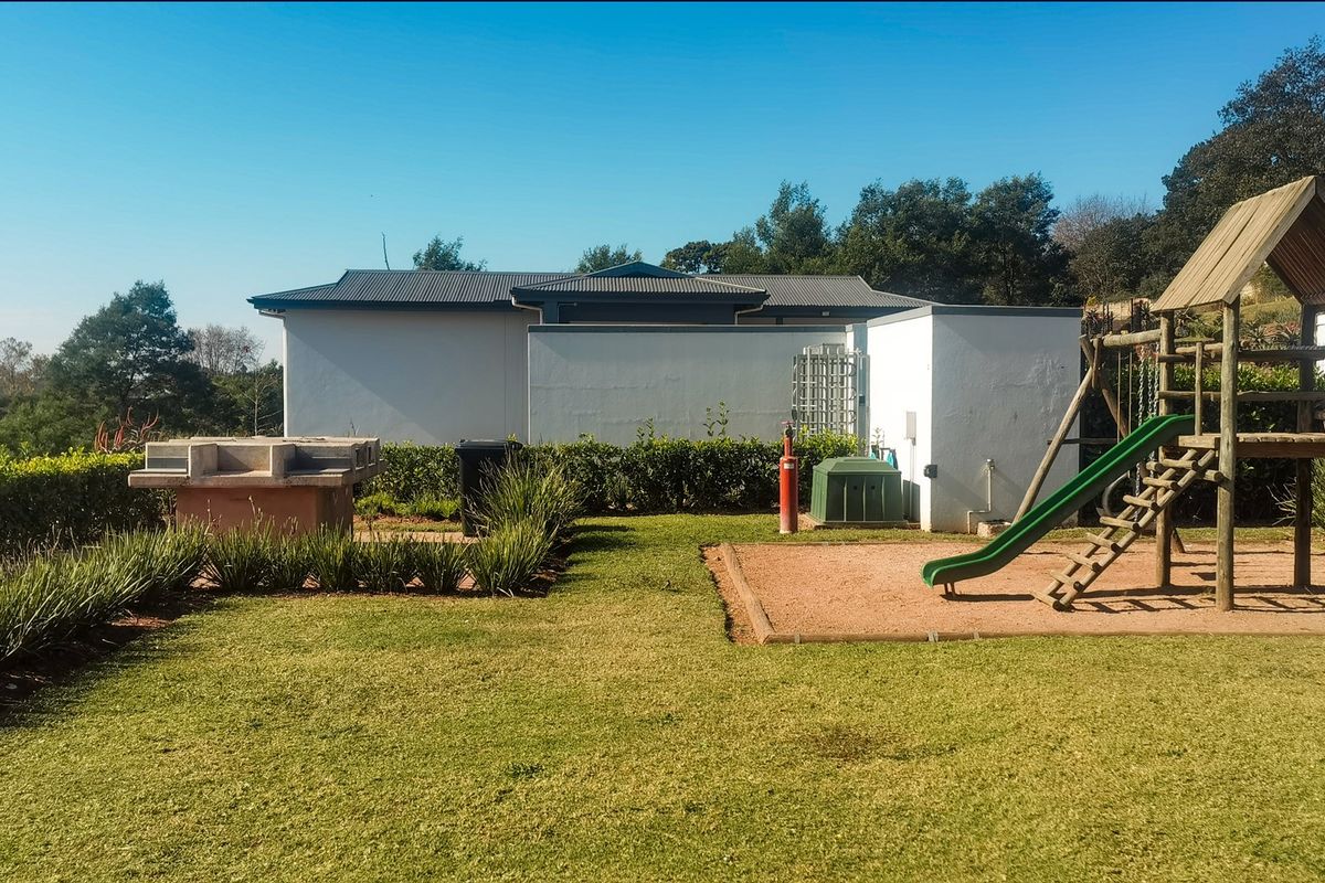 Rear garden area featuring a built-in braai, manicured lawn, and children's playground equipment set against a clear sky.