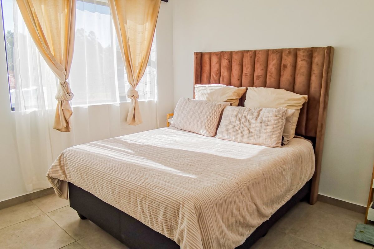 A well-lit bedroom featuring neutral tones, tiled flooring, and a large window allowing for ample natural light.