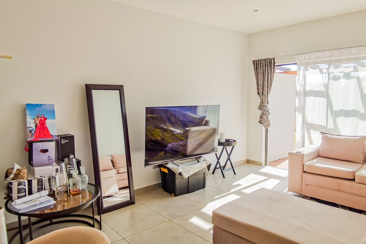 A bright living room featuring neutral tiled flooring and a sliding glass door providing access to an outdoor area.