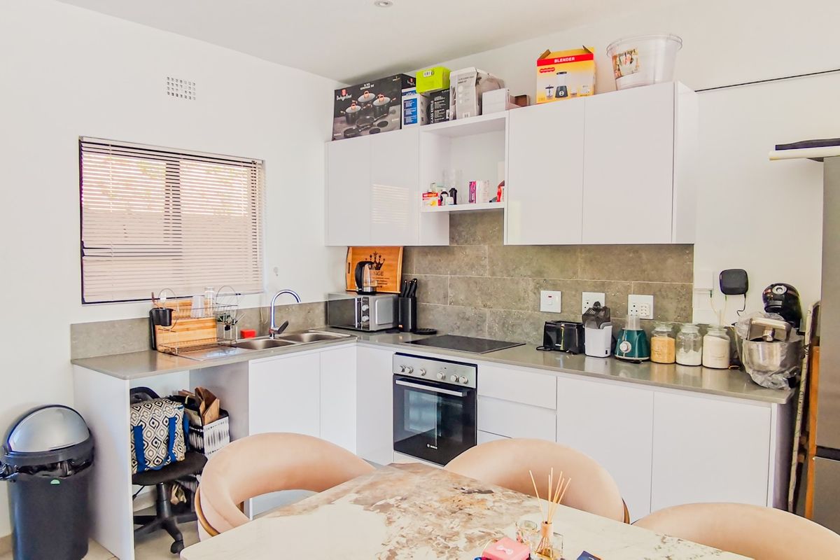 A functional kitchen featuring white cabinetry, stone-look backsplash, integrated oven and hob, and ample countertop space.