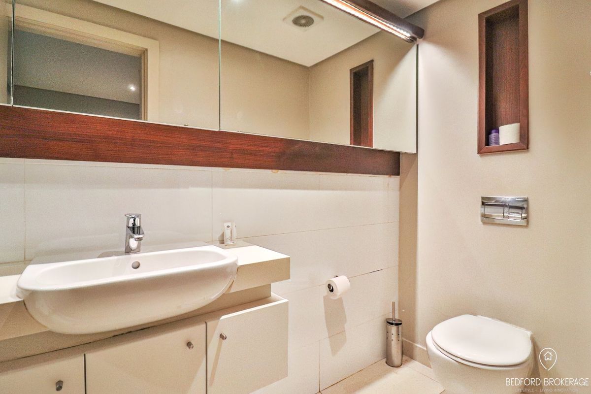 Modern bathroom featuring a wall-hung toilet, vanity cabinet with integrated basin, and a large wall-mounted mirror with recessed shelving.