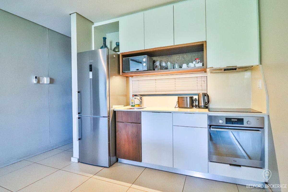 Compact modern kitchen featuring sleek cabinetry, integrated stainless steel appliances, built-in oven, electric cooktop, and tiled flooring.