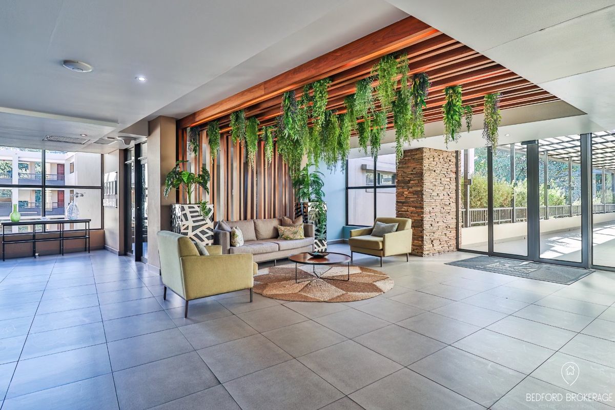 Modern apartment lobby or living area featuring a striking timber slat ceiling, stone feature wall, and large glass doors leading to an outdoor space.