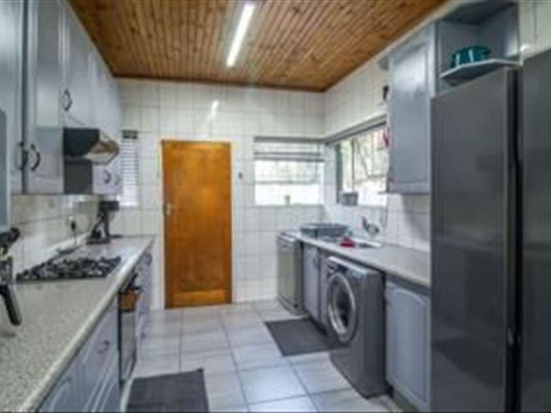 Functional kitchen featuring built-in cabinetry, gas hob, extractor fan, and tiled finishes with a timber ceiling.