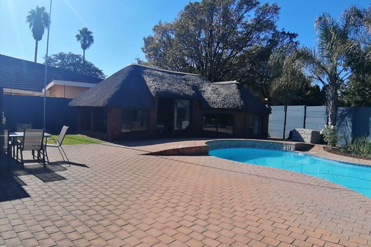 Outdoor entertainment area featuring a swimming pool, brick-paved patio, and a traditional thatched-roof lapa structure.