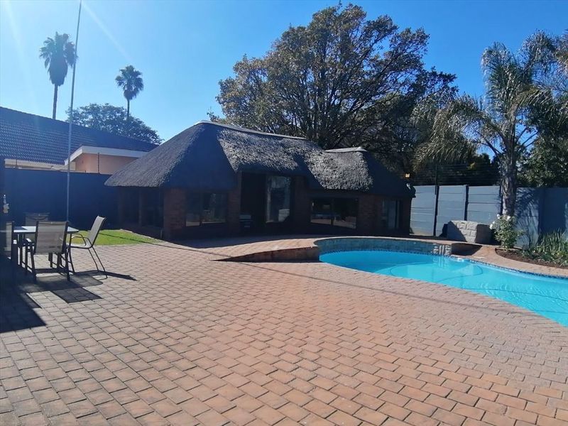 Outdoor entertainment area featuring a swimming pool, brick-paved patio, and a traditional thatched-roof lapa structure.